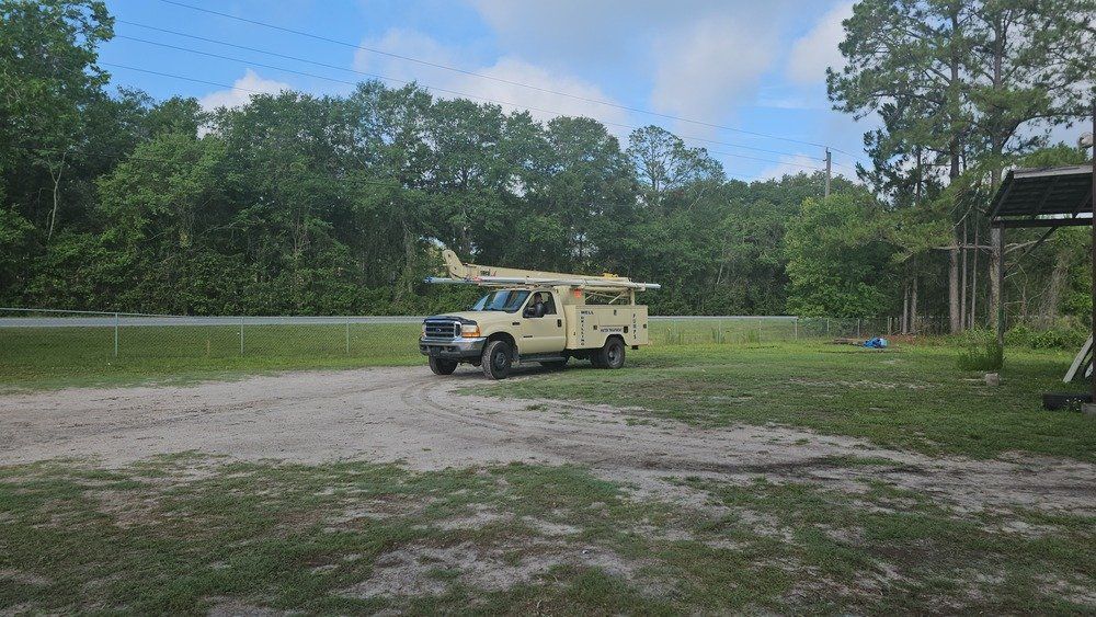 A yellow truck is parked in a dirt lot next to a road.