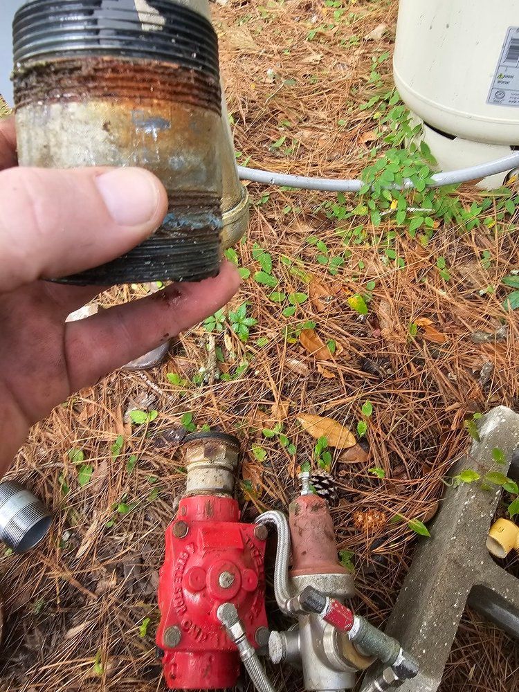 A person is holding a metal object in their hand next to a red valve.