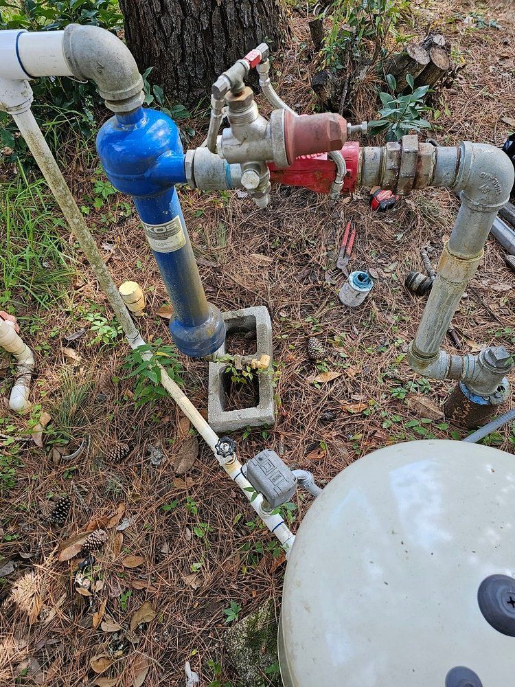 A bunch of pipes are sitting on the ground next to a water tank.