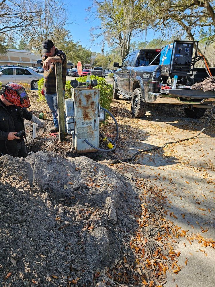 A man is welding a pole in the dirt next to a truck.