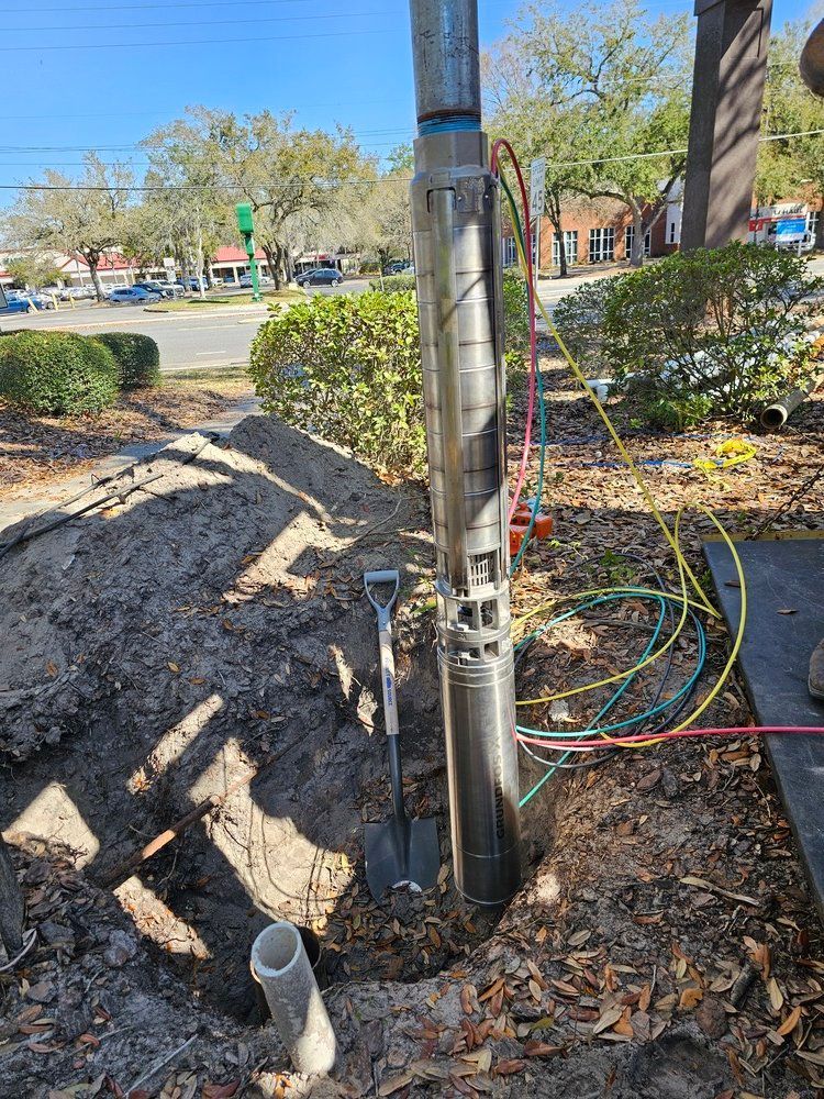 A water pump is being installed in the ground next to a hose and a shovel.