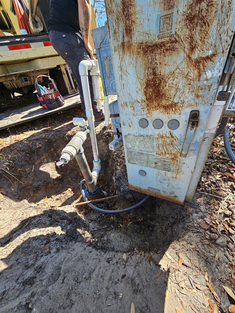 A man is working on a rusty machine in the dirt.