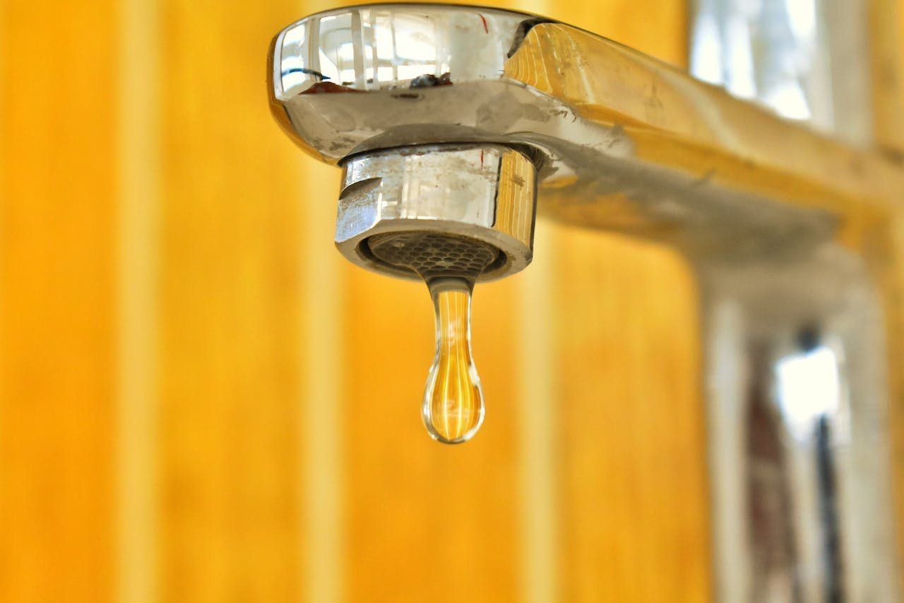 A close up of a faucet with a drop of water coming out of it.