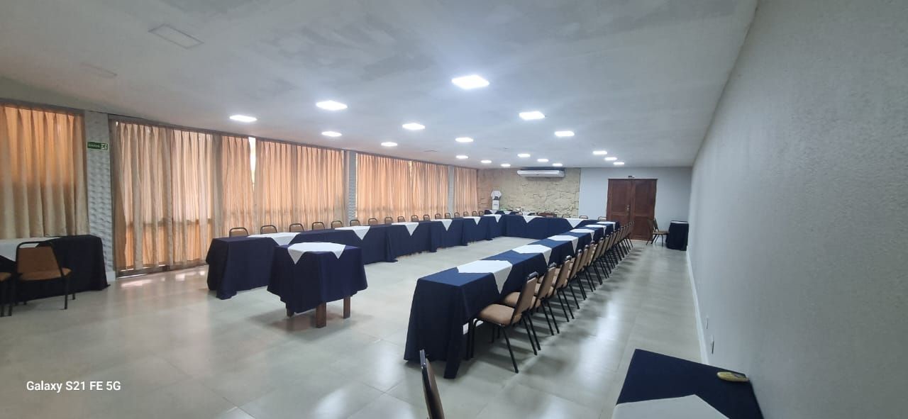 Uma sala de conferências com mesas cobertas por toalhas azul-escuras. Cortinas bege revestem a parede curva.