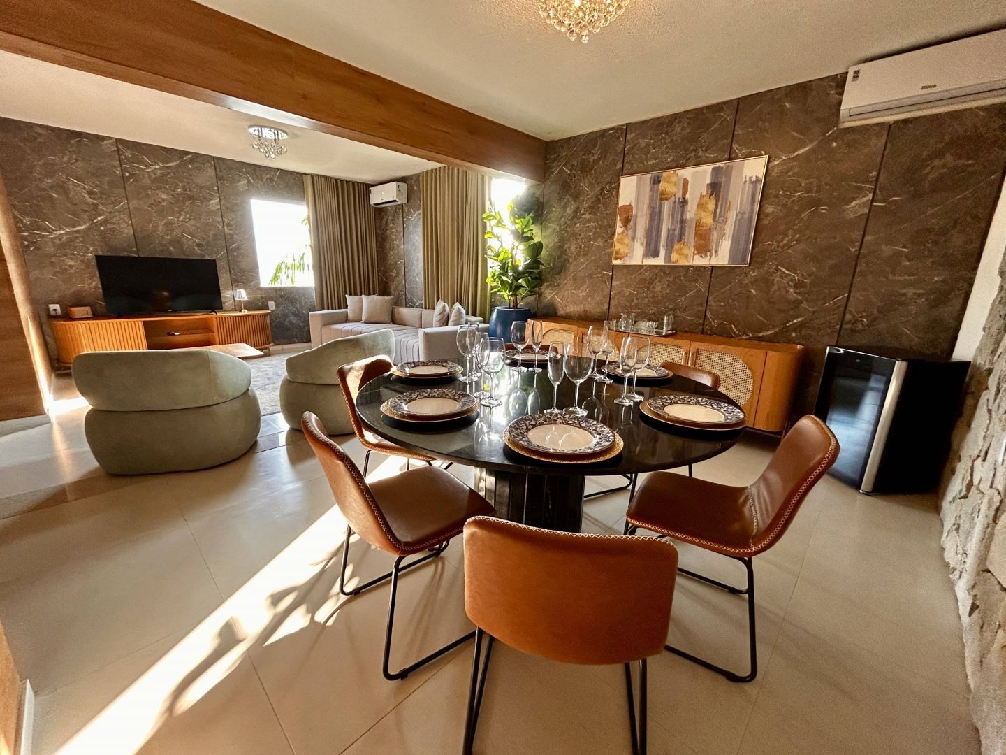 Sala de jantar com mesa redonda para seis pessoas, adjacente a uma sala de estar com sofá e televisão.