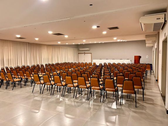 Sala de eventos vazia com fileiras de cadeiras voltadas para um palco com pódio.