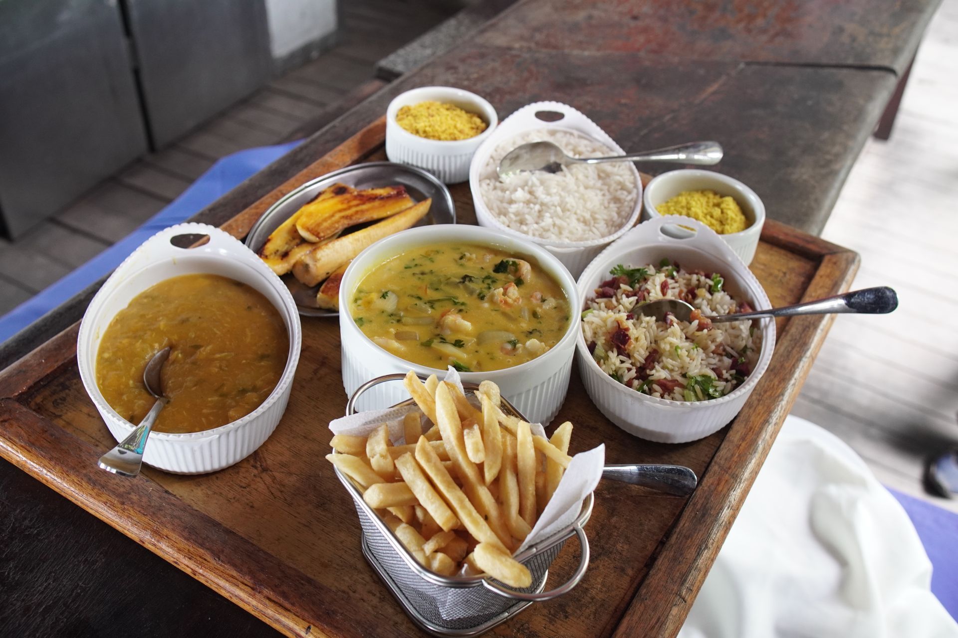 Bandeja com diversos pratos brasileiros, incluindo arroz, ensopado e batatas fritas.