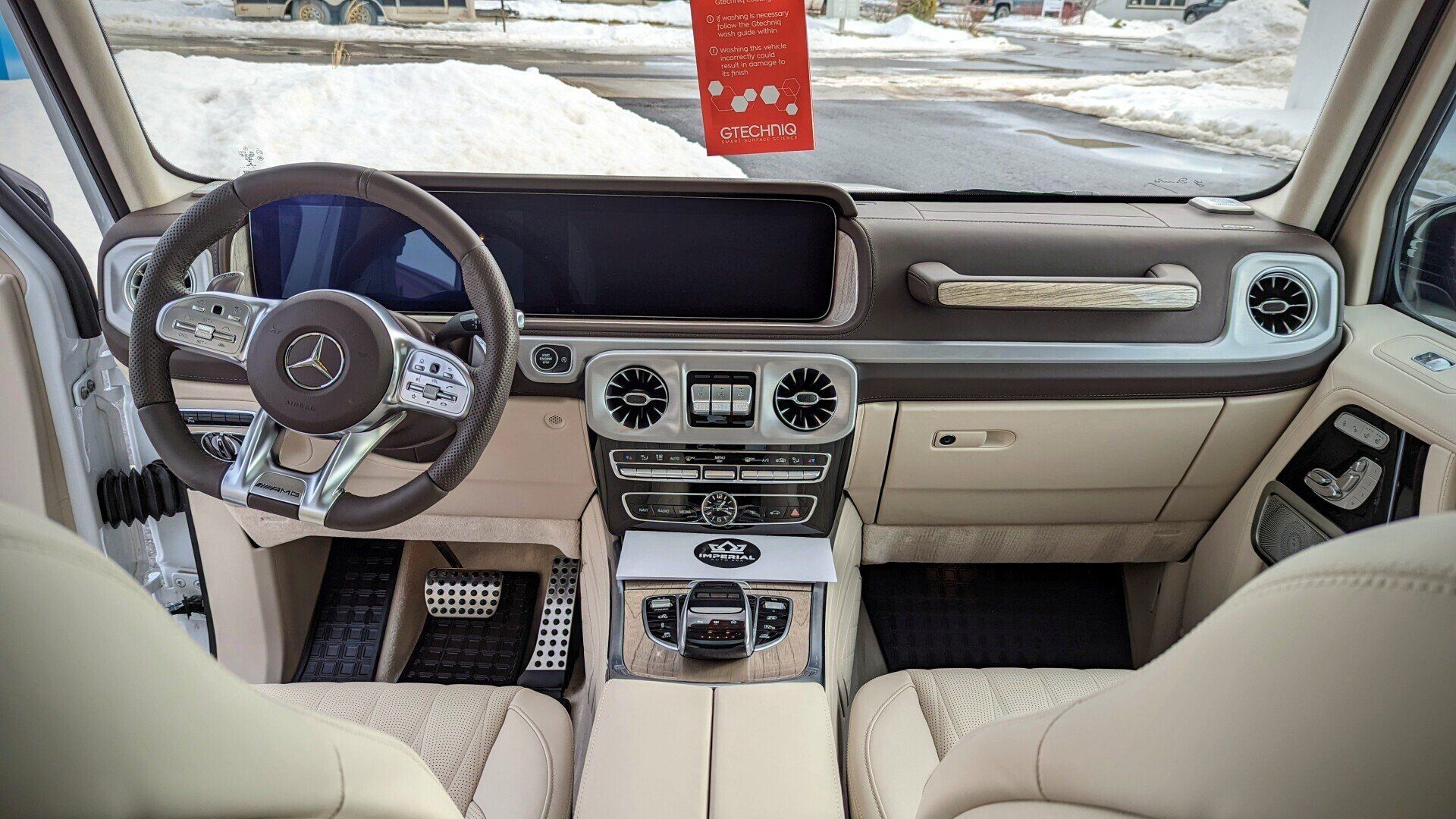 Interior view of a beige and brown Mercedes-Benz G-Class SUV, chrome and wood accents, snowy exterior.
