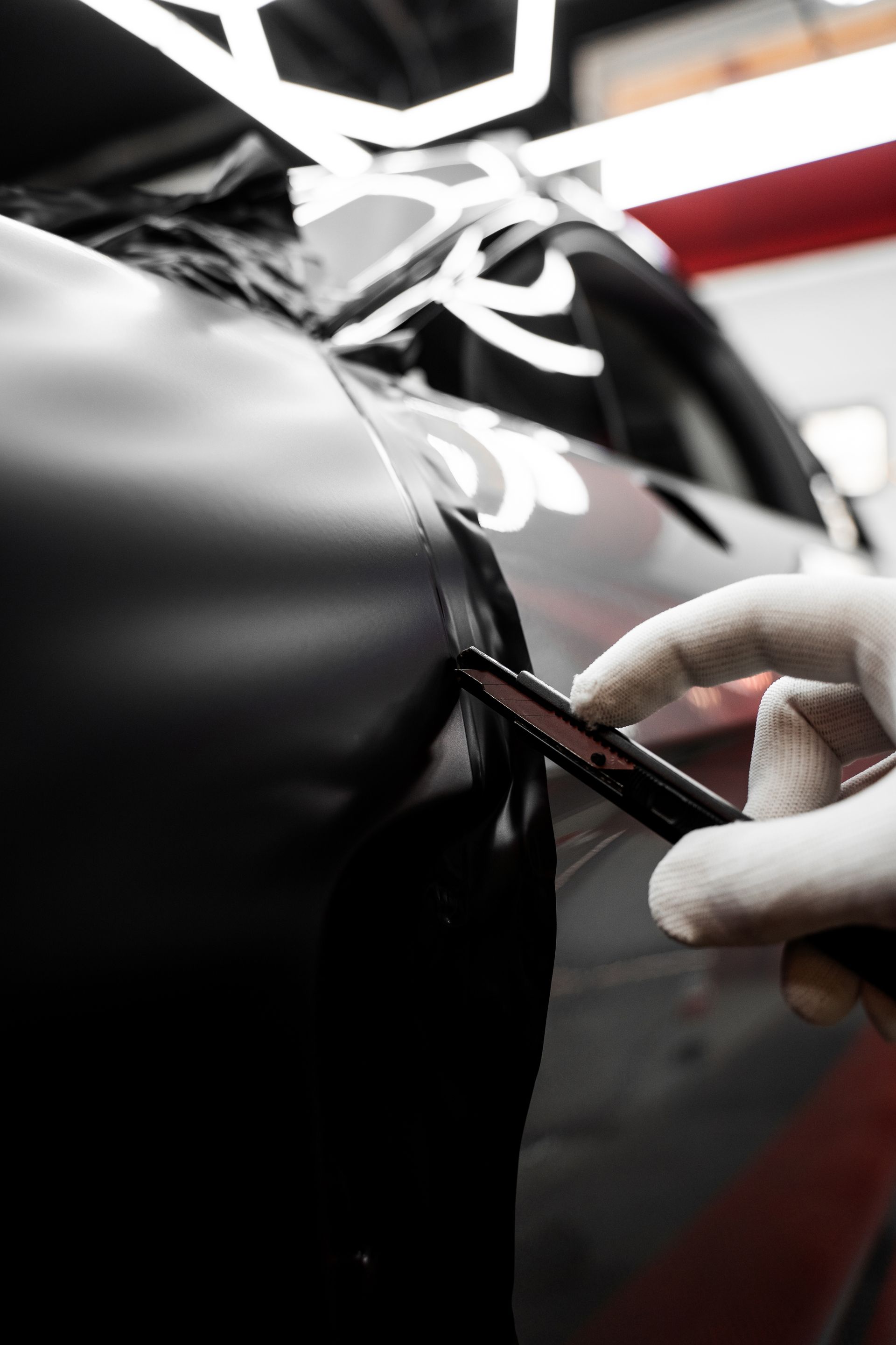 Gloved hand applying vinyl wrap to a glossy black car panel with a squeegee