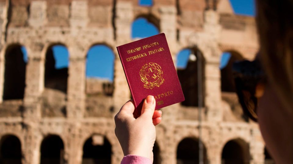 Mão segurando um passaporte italiano em frente ao Coliseu de Roma