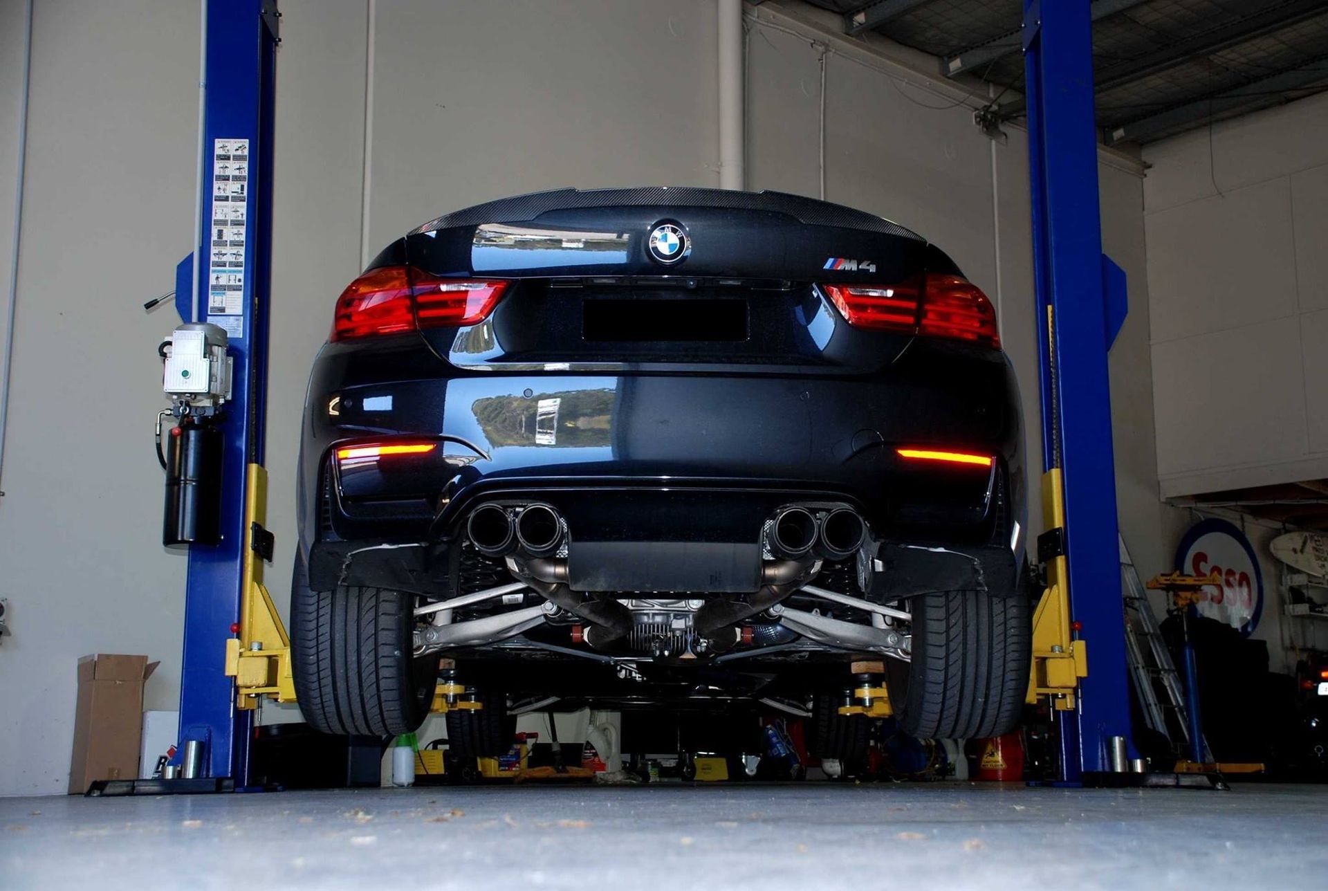 A black bmw is on a lift in a garage. — Queensland Roadworthy Services In Southport, QLD