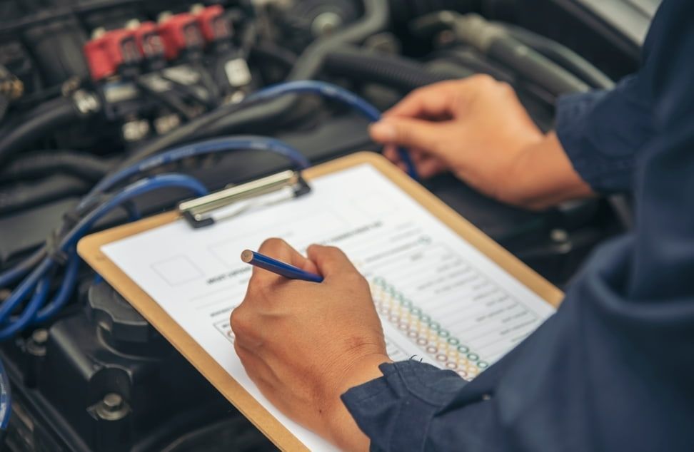 A Mechanic is Writing on a Clipboard While Working on a Car — Queensland Roadworthy Services In Southport, QLD