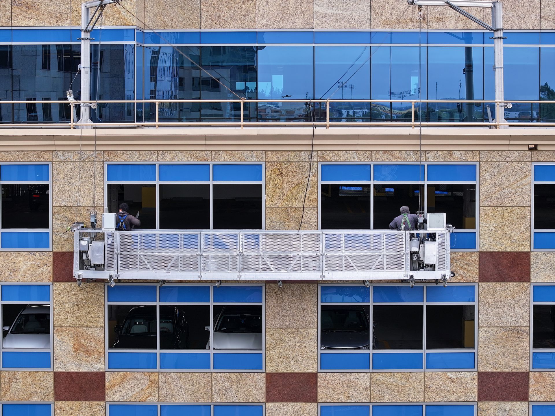 Workers in a suspended platform washing windows of a building with blue-tinted windows.