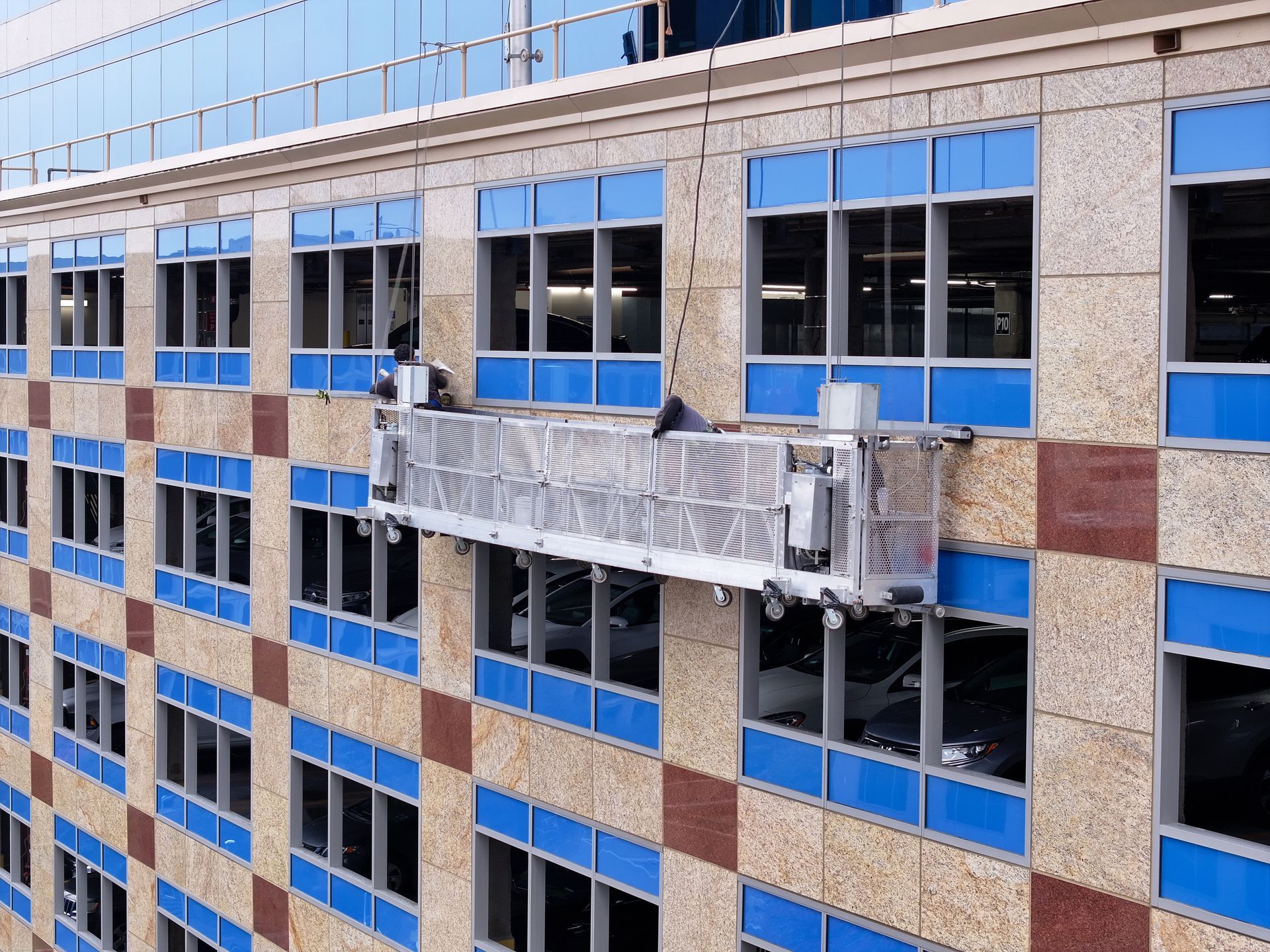 Workers on a suspended platform cleaning windows of a multi-story building.
