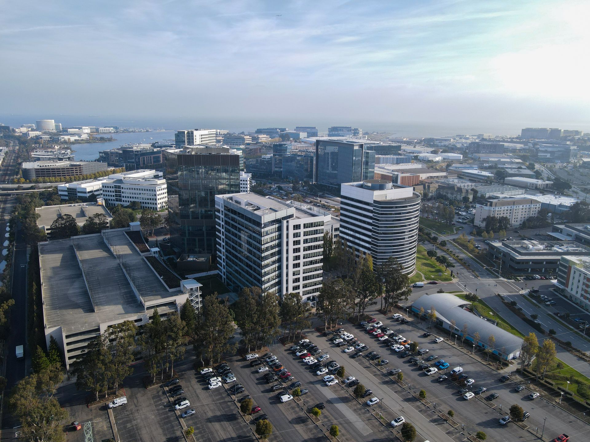 Aerial view of buildings, parking lot, and harbor on a sunny day.