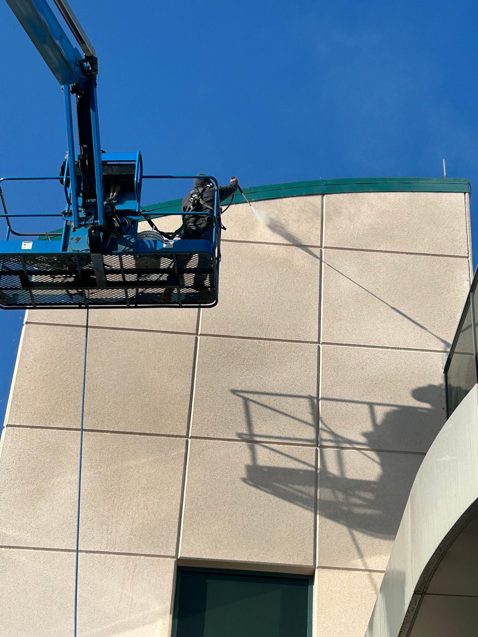 Blue lift platform by a beige building, person visible working on the roof under a blue sky.