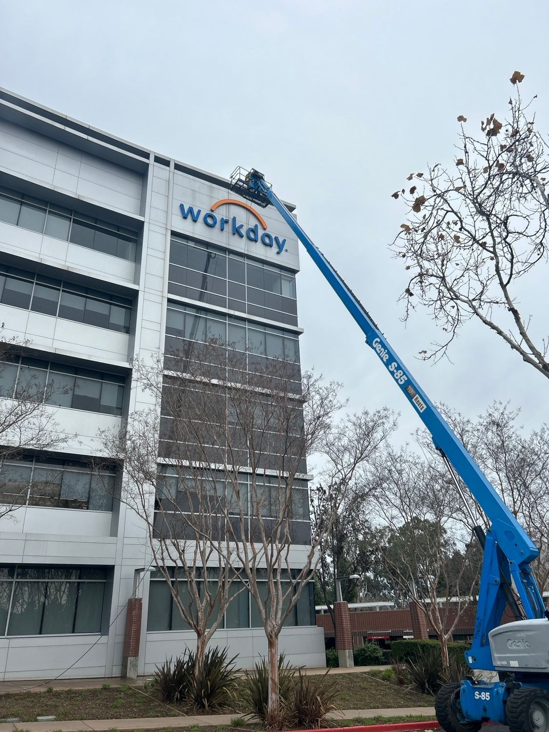 A blue lift truck near a building with the Workday logo, possibly installing the sign on the building.