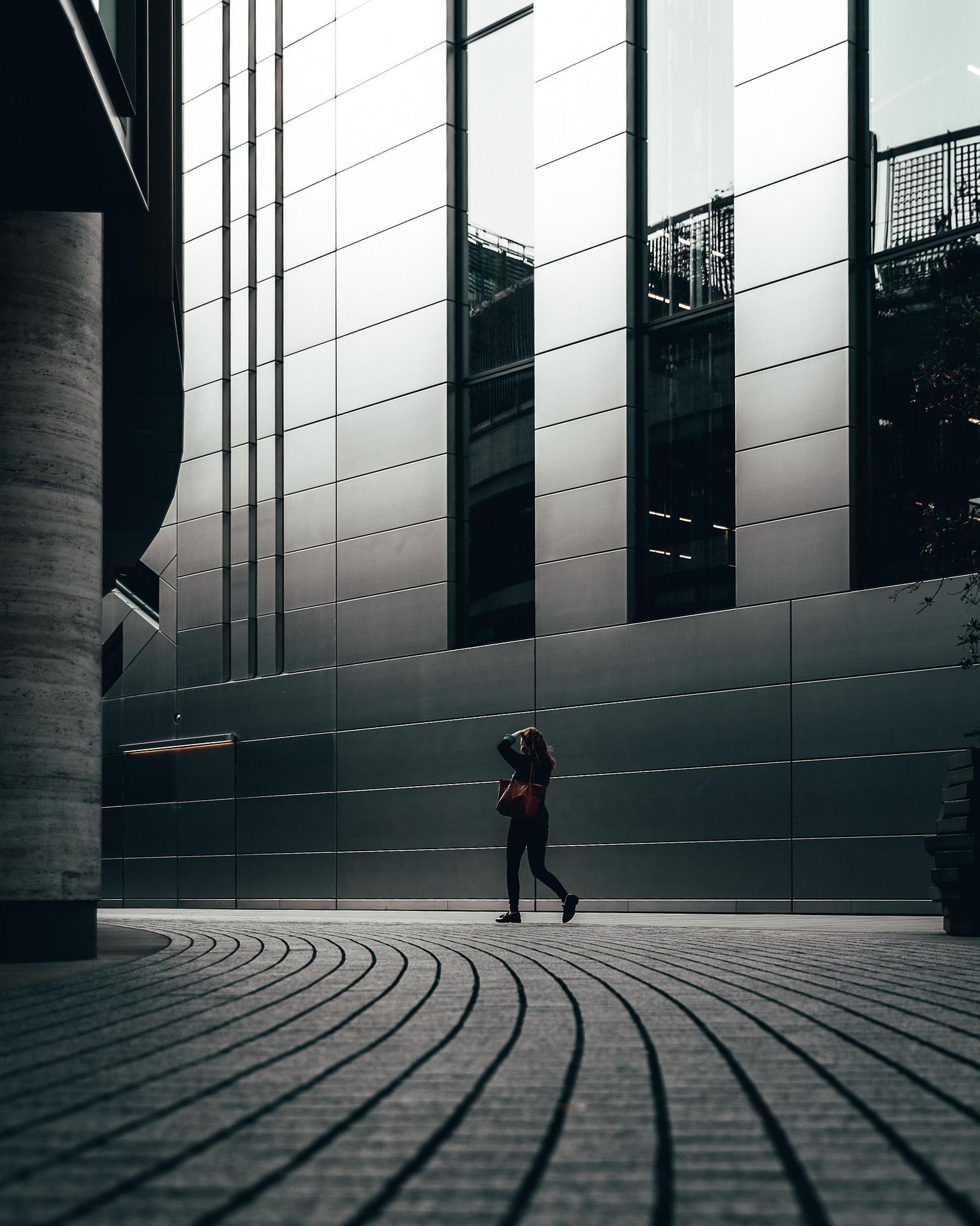 Person walking in modern architectural courtyard, reflective building facade behind.