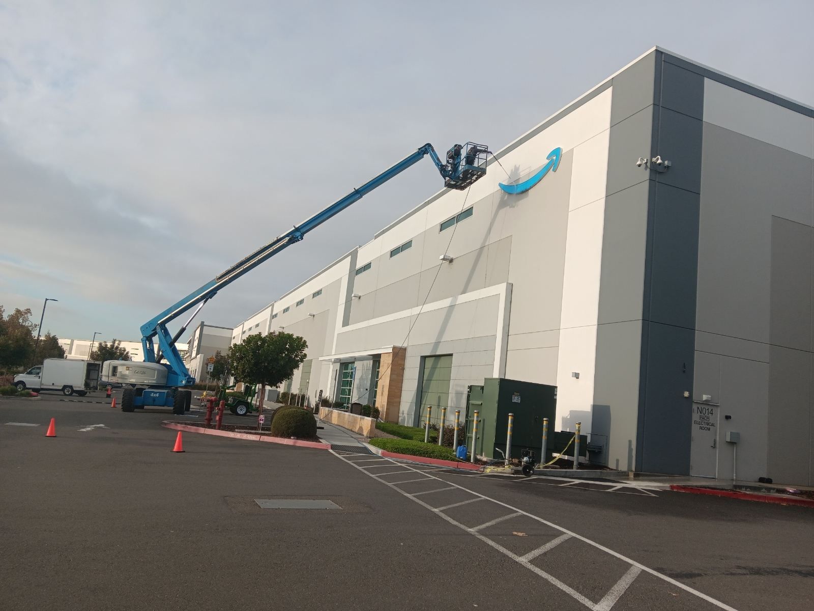 A blue lift truck with workers installing a logo on a large building. Outdoor setting, gray and blue color scheme.