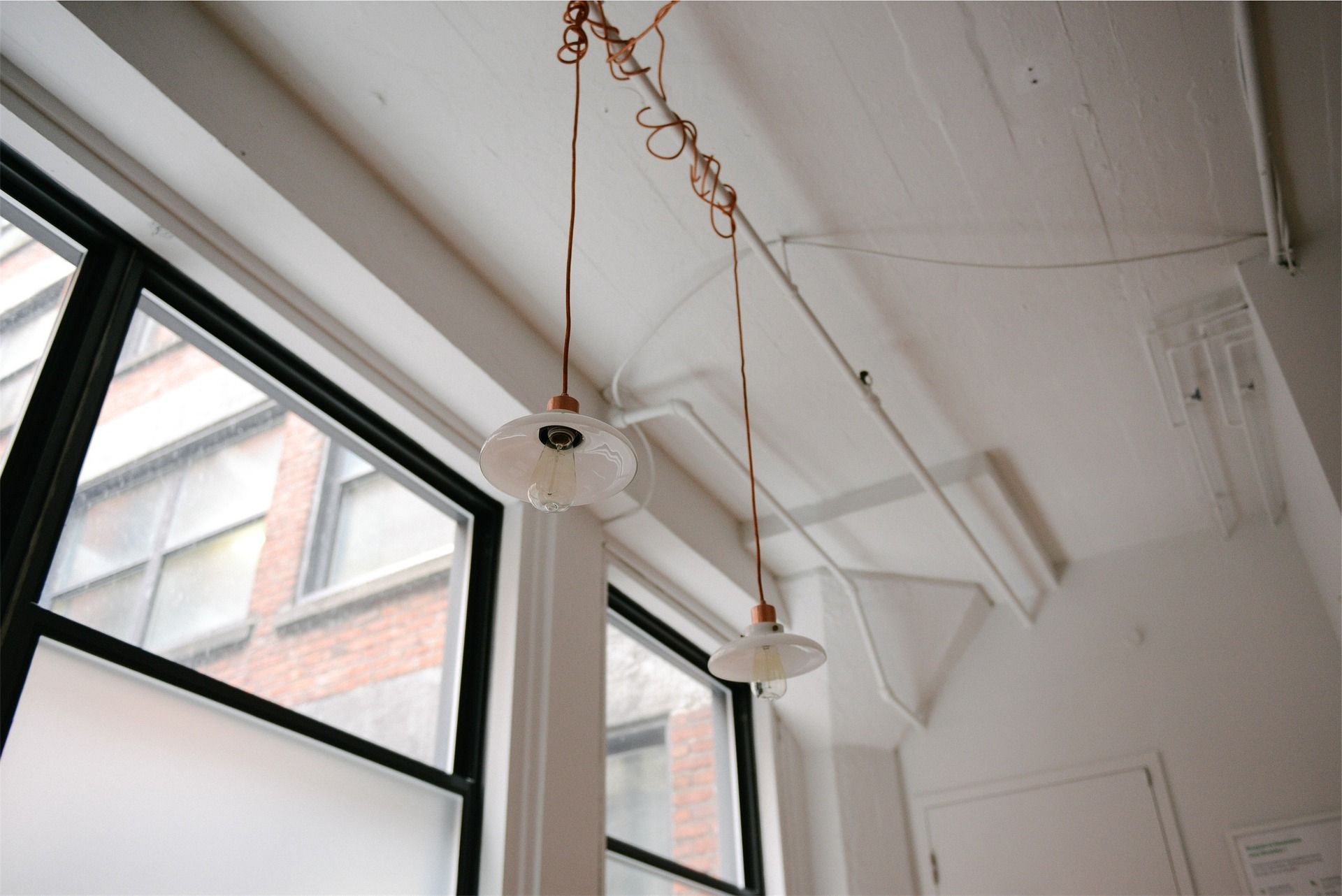 Two pendant lights hang from a white ceiling near a large window.