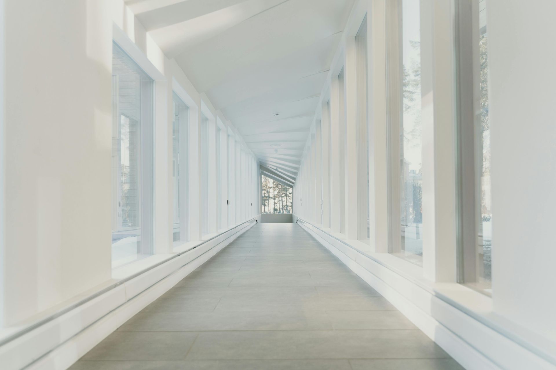 Bright white interior hallway with windows on both sides, leading to a distant view.