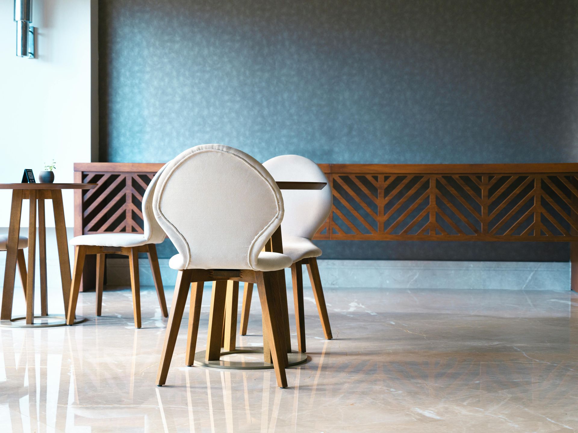 Wooden chairs and table against a patterned wall, with a marble floor.