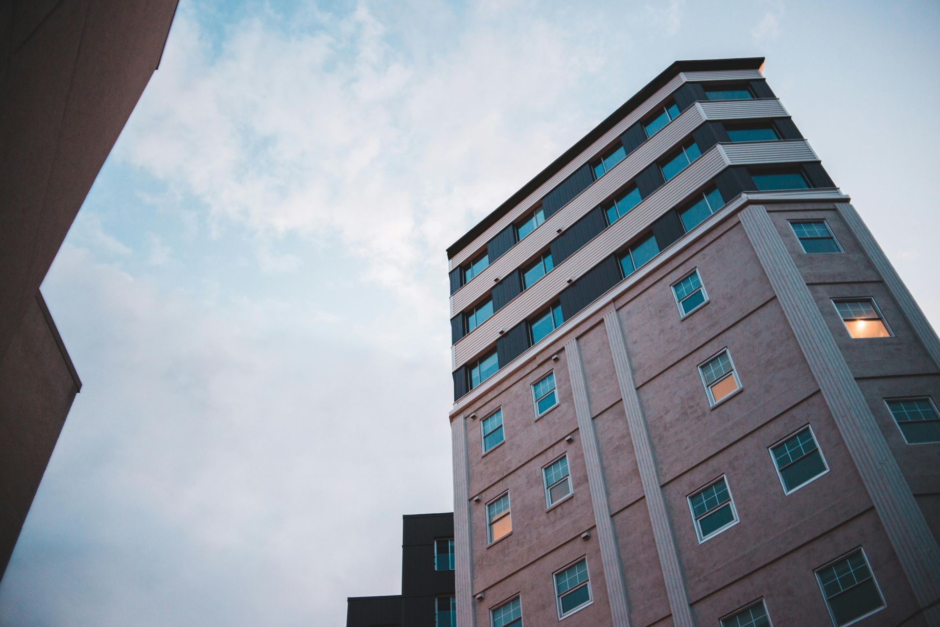 Low-angle view of a tall brick building against a cloudy sky; several windows are lit up.