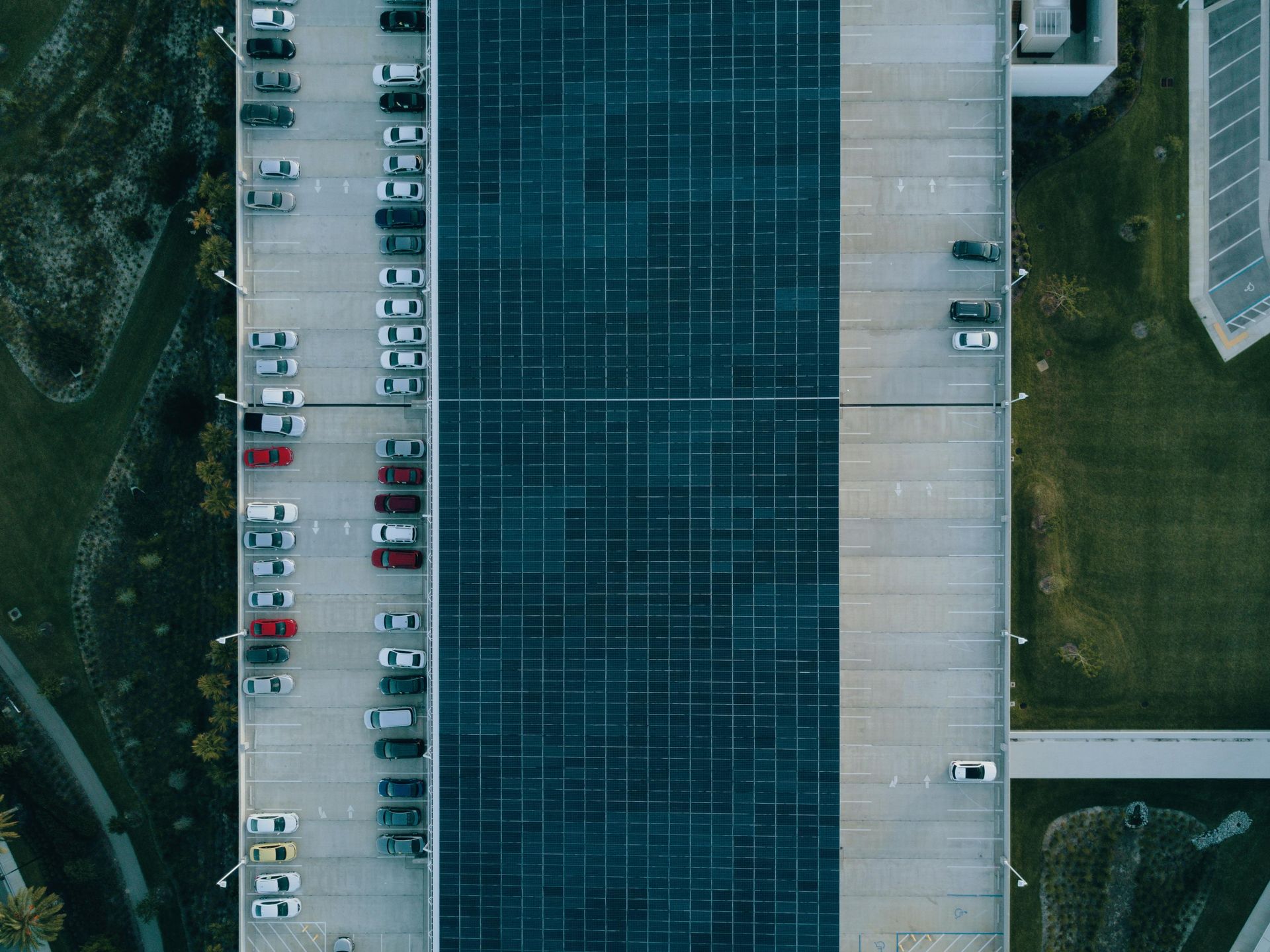 Aerial view of a parking garage filled with cars, with green landscaping along the edges and a rooftop.