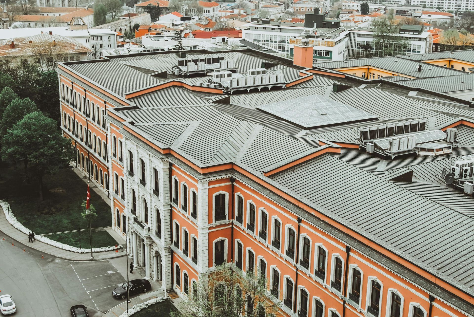 Large, ornate building with a red-orange facade and a gray, multi-layered roof, in an urban setting.