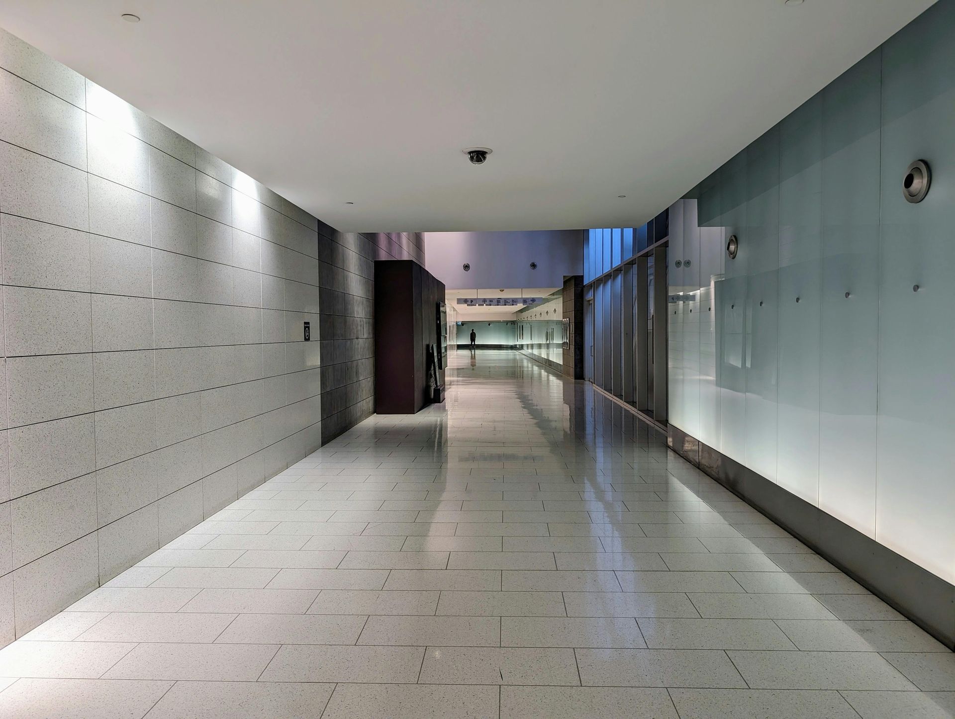 Hallway with white tile floor, gray tiled left wall, glass right wall.