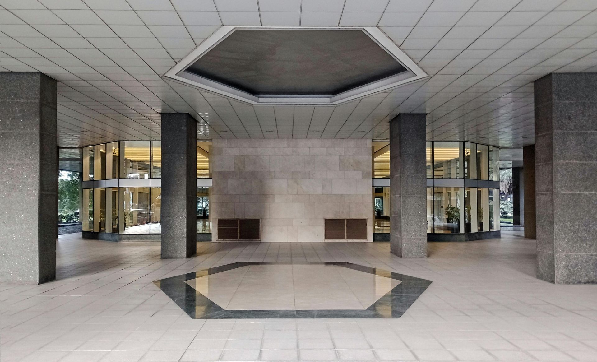 Entrance to a building with granite pillars, glass doors, and a hexagonal design on the ceiling and floor.