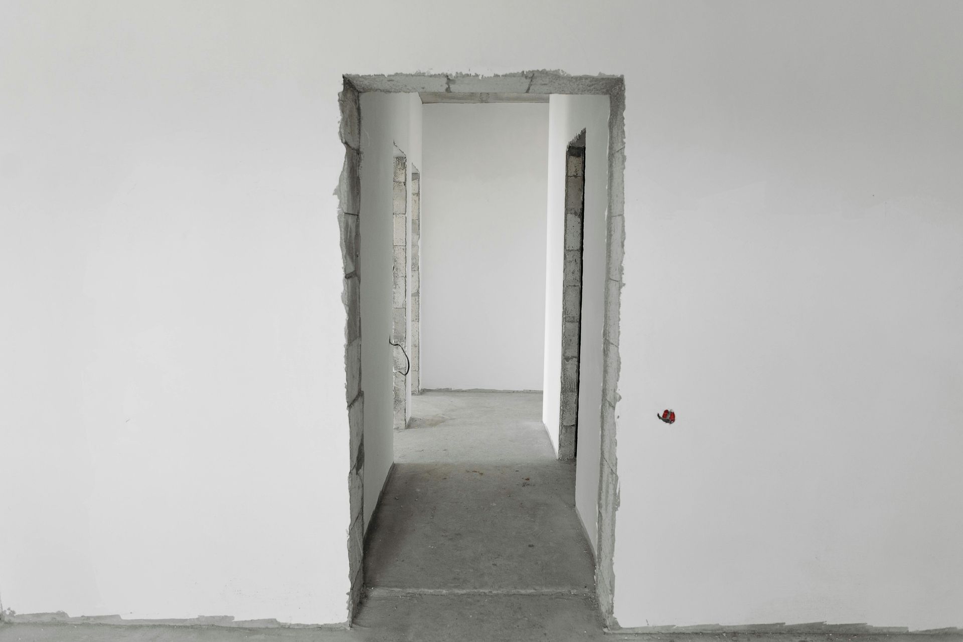 Interior with unfinished white walls, open doorway leading to a hallway with a concrete floor.
