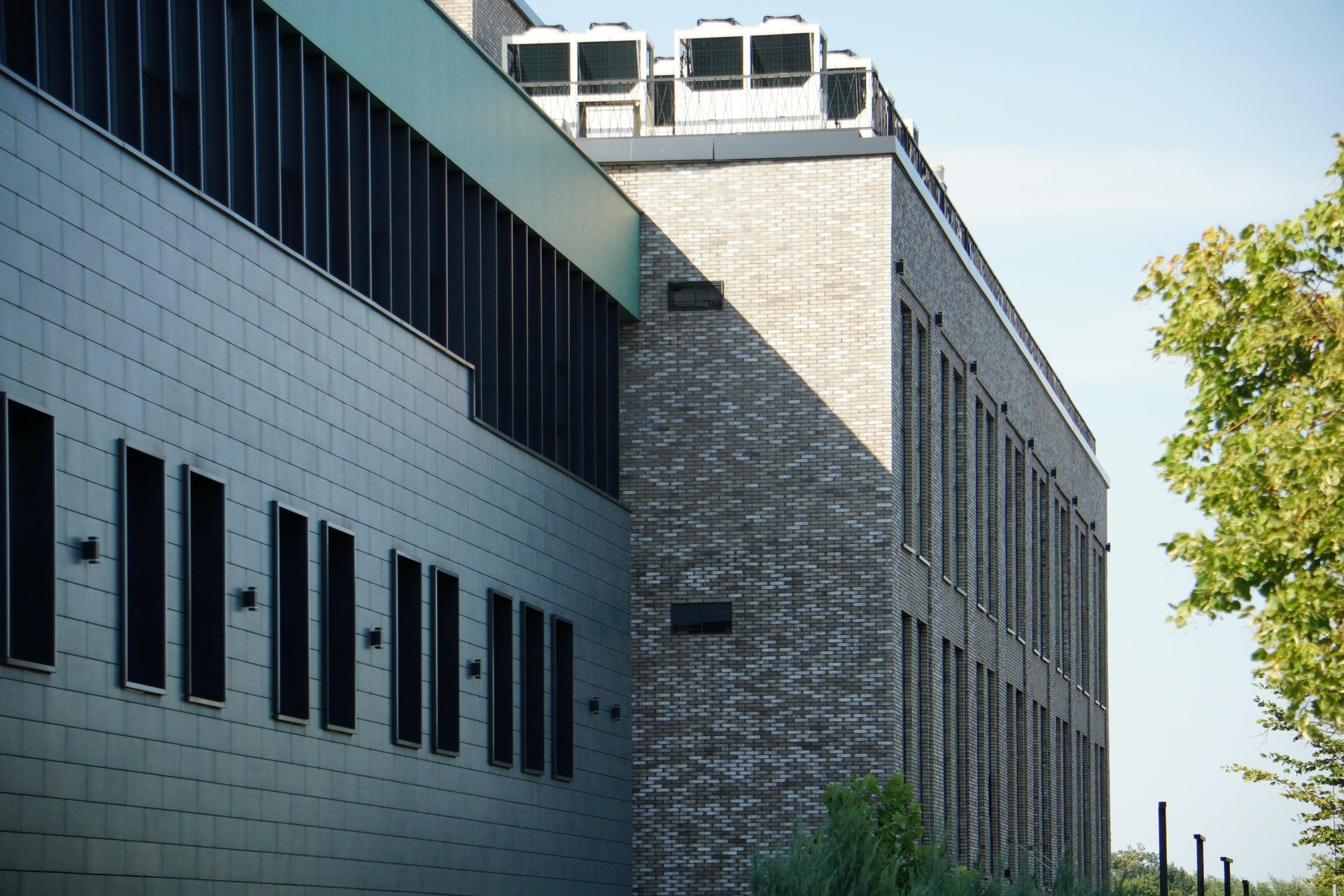 Modern brick and gray building with vertical windows and rooftop HVAC units.