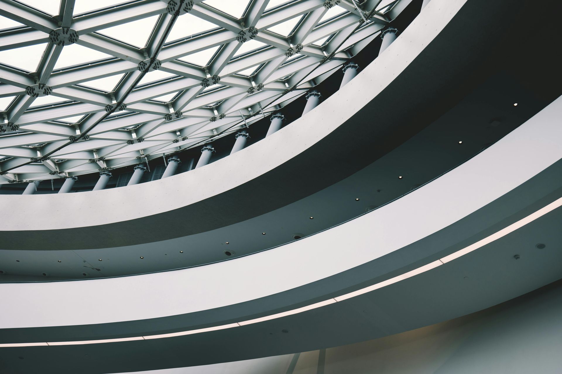 Interior view of a modern building with curved white and gray walls, and a glass triangular ceiling.