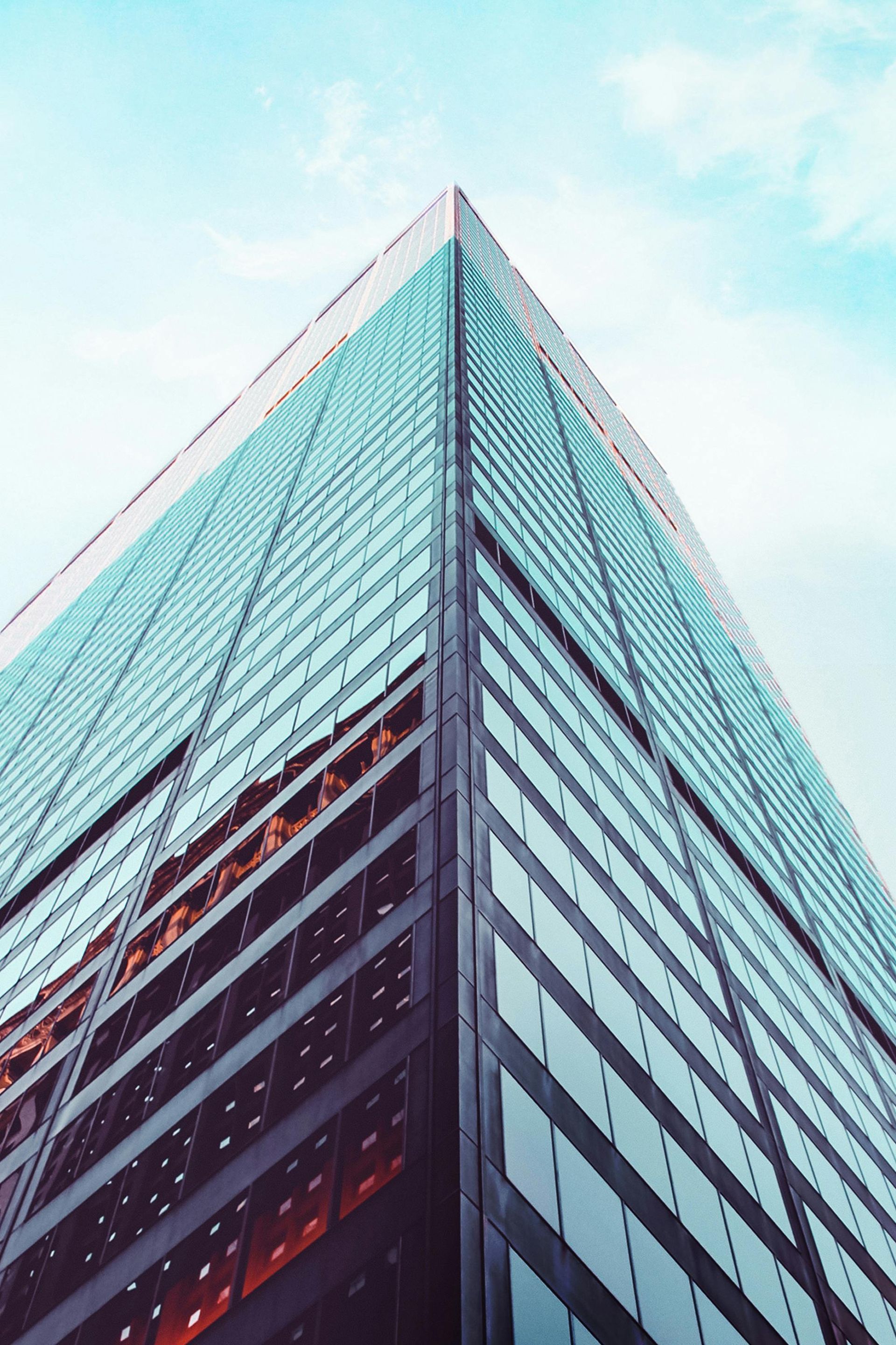 Tall glass skyscraper, blue windows, angled view upward against a light blue sky.