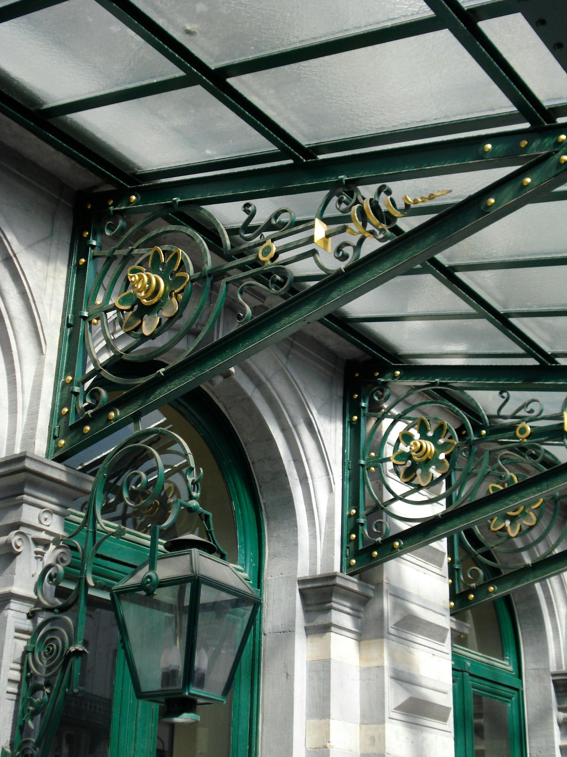 Green and gold ornate metalwork canopy over a building entrance with a lamp.
