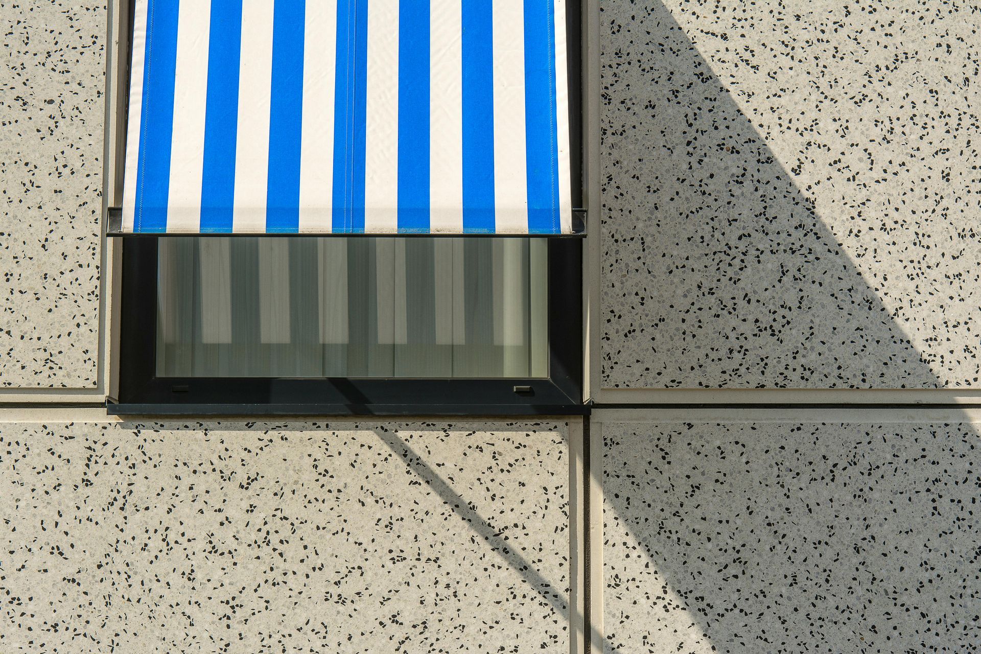 Blue and white striped awning shading a window in a speckled concrete wall.
