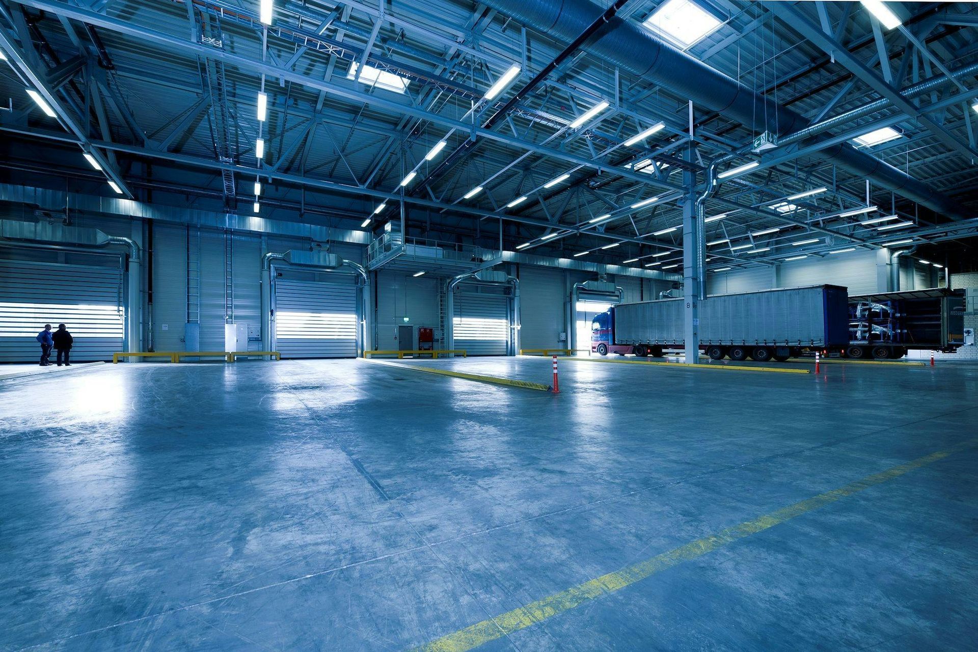 Large warehouse interior with loading docks and trucks; cool blue tones.