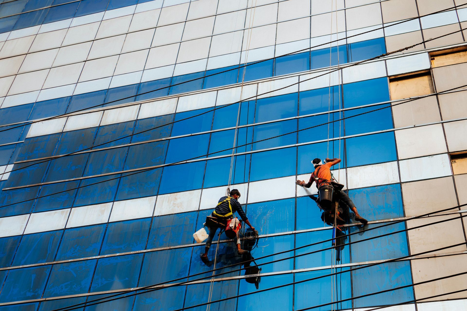 Two window washers on ropes cleaning a blue and white glass skyscraper.