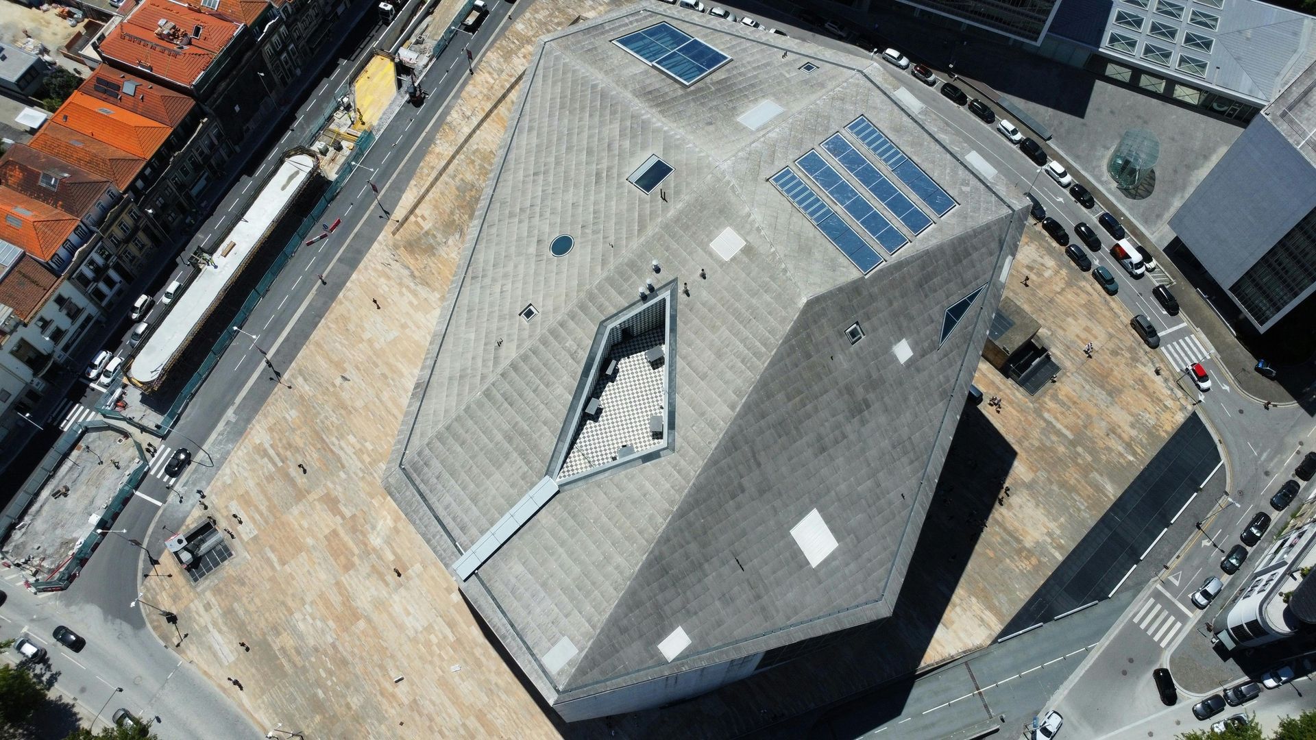 Aerial view of a modern building with a geometric roof in an open square.