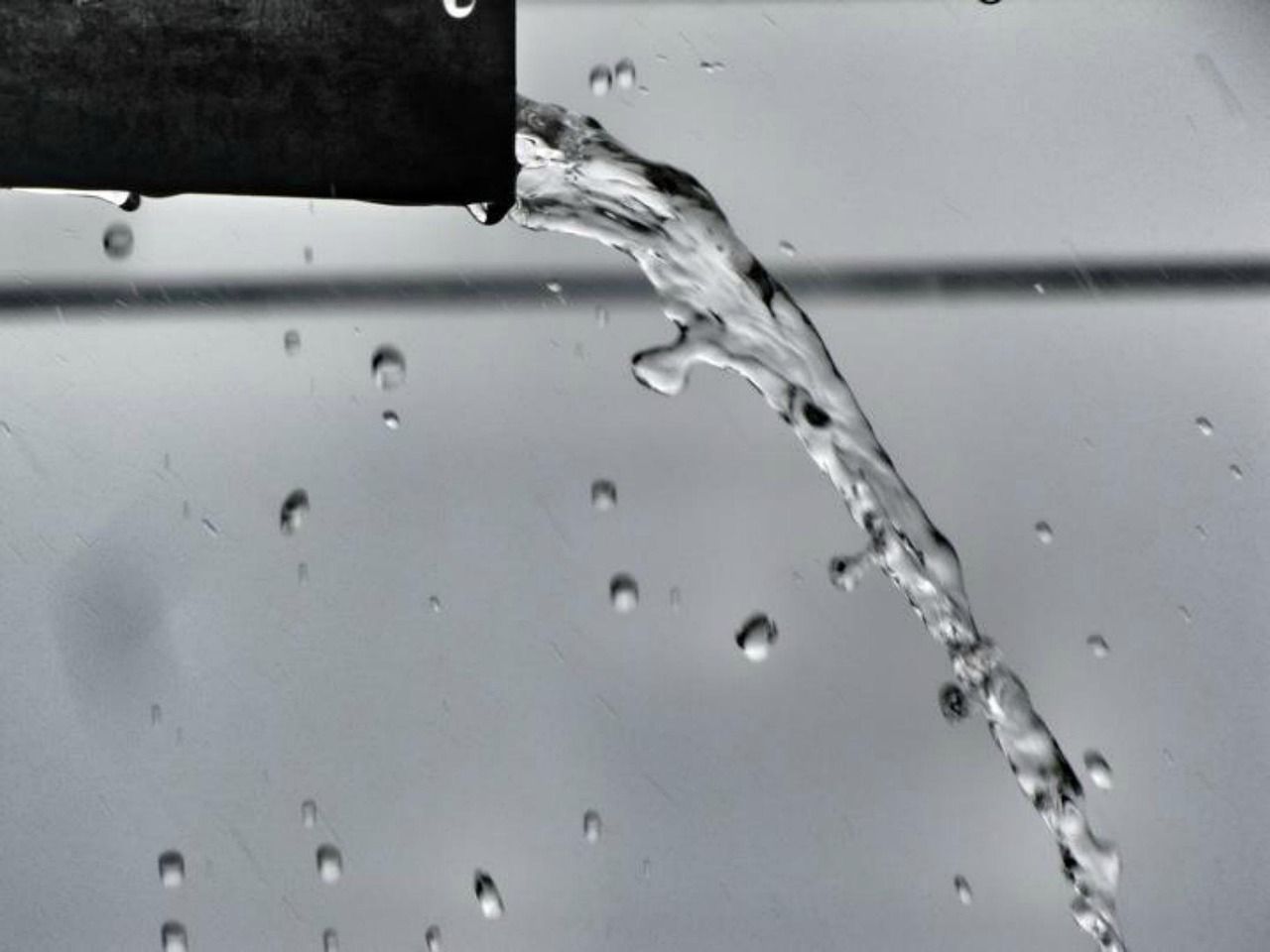 Water pouring from a black pipe, droplets and stream against a gray background.
