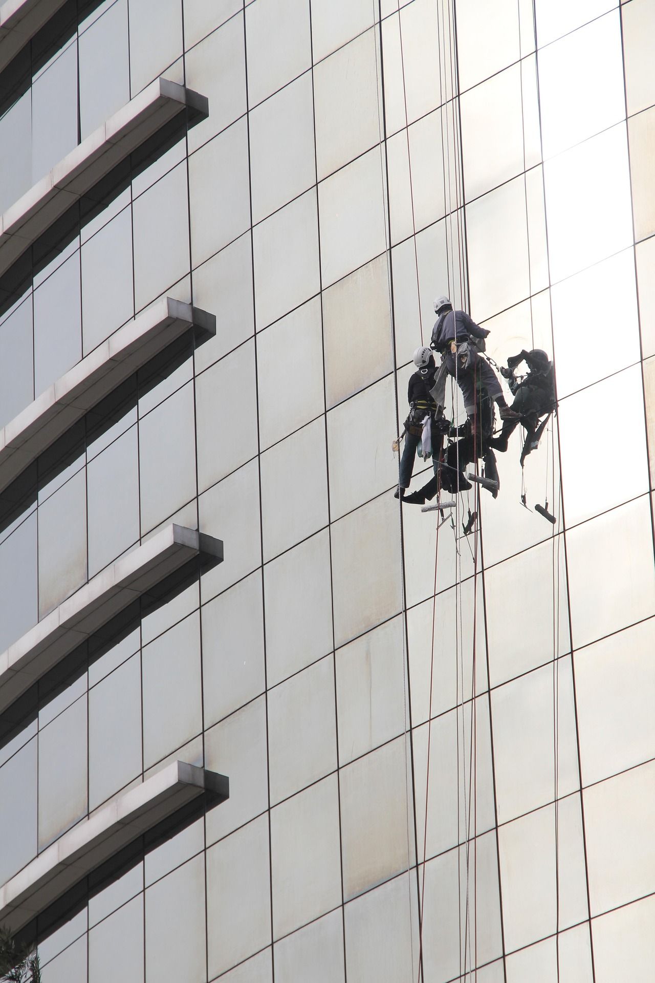 Window washers suspended on a high-rise building, cleaning reflective glass panels.