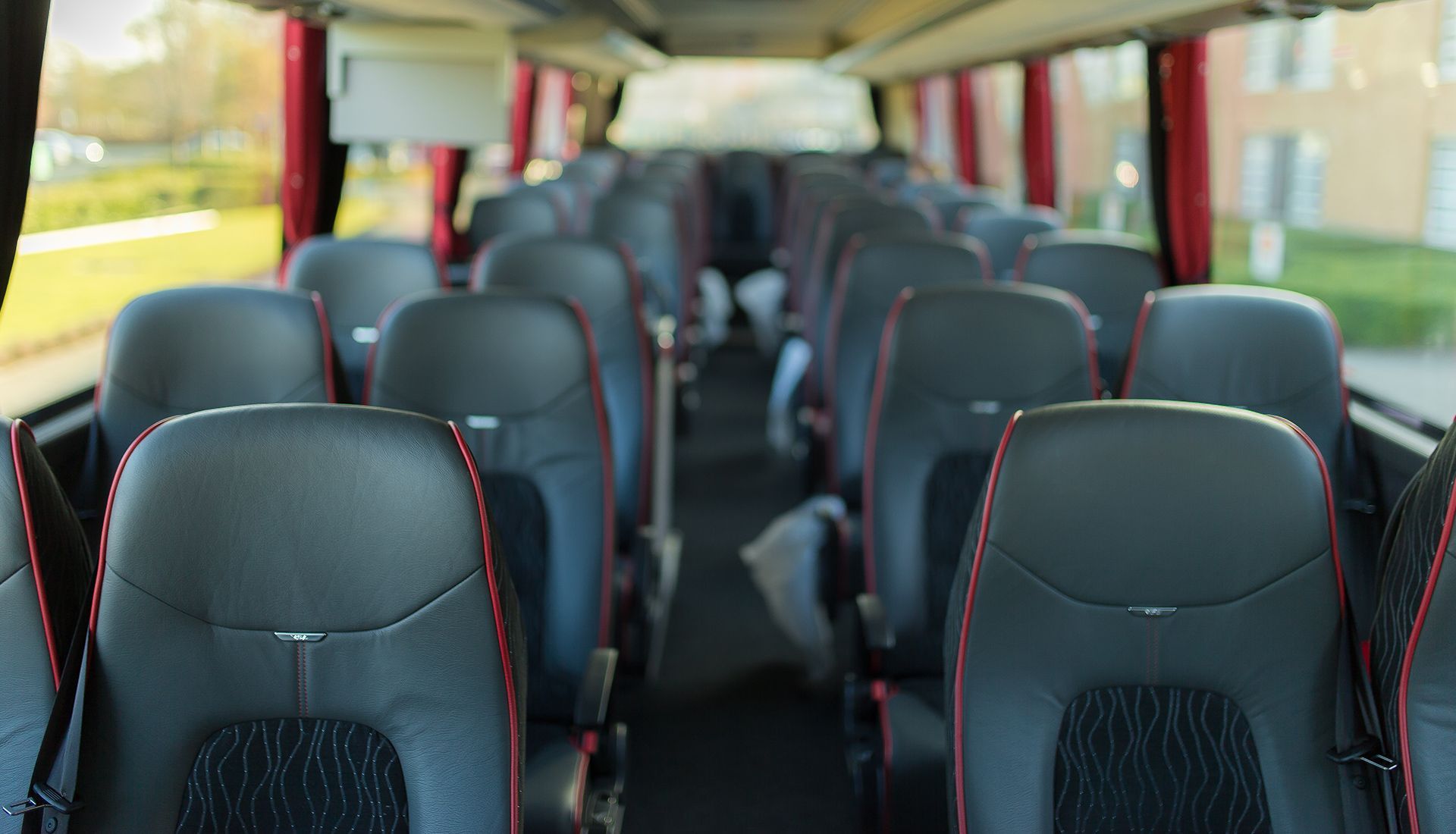 Interior of a bus, black leather seats with red trim, aisle down the center.