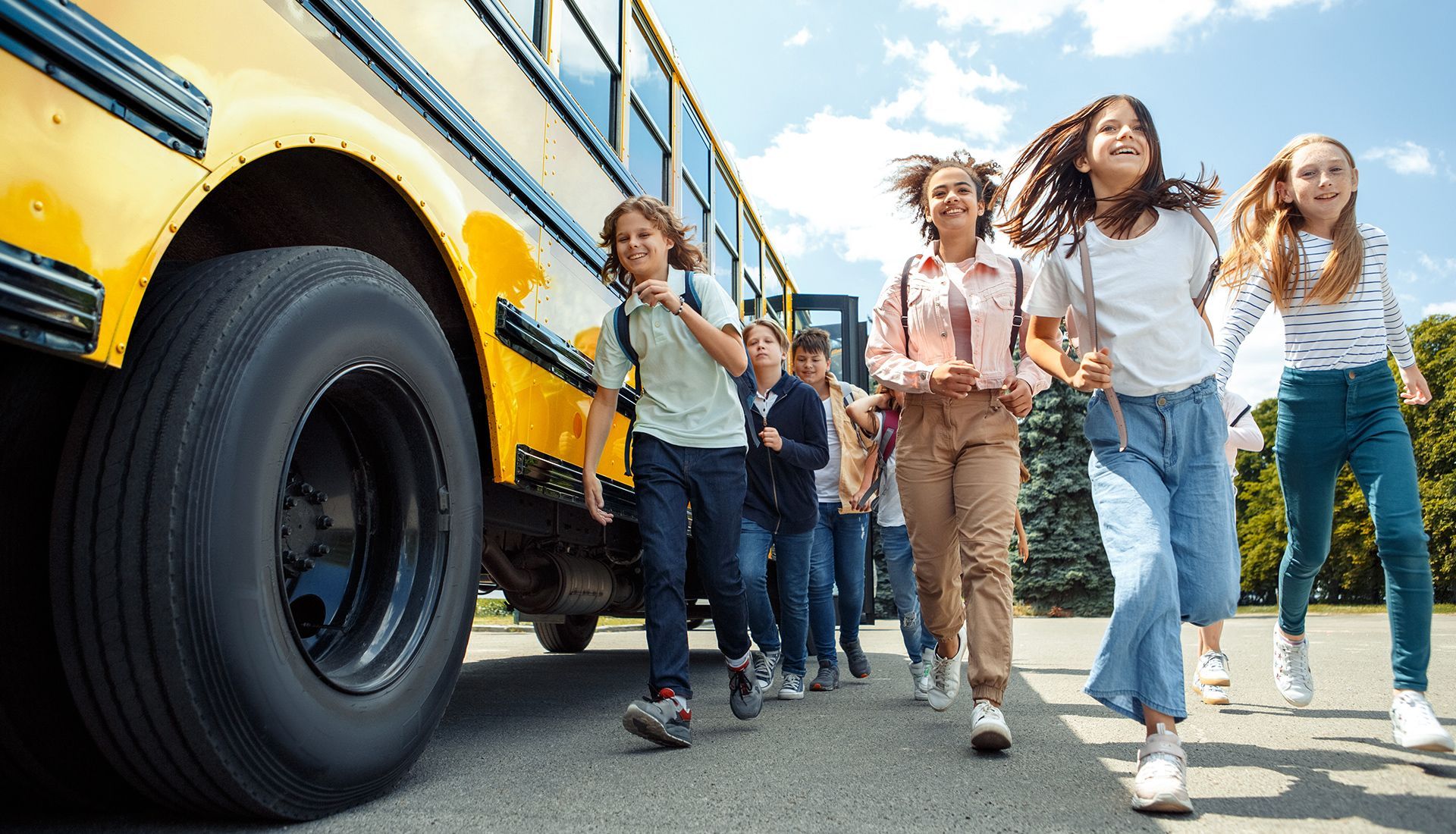 School children running from a yellow school bus on a sunny day.