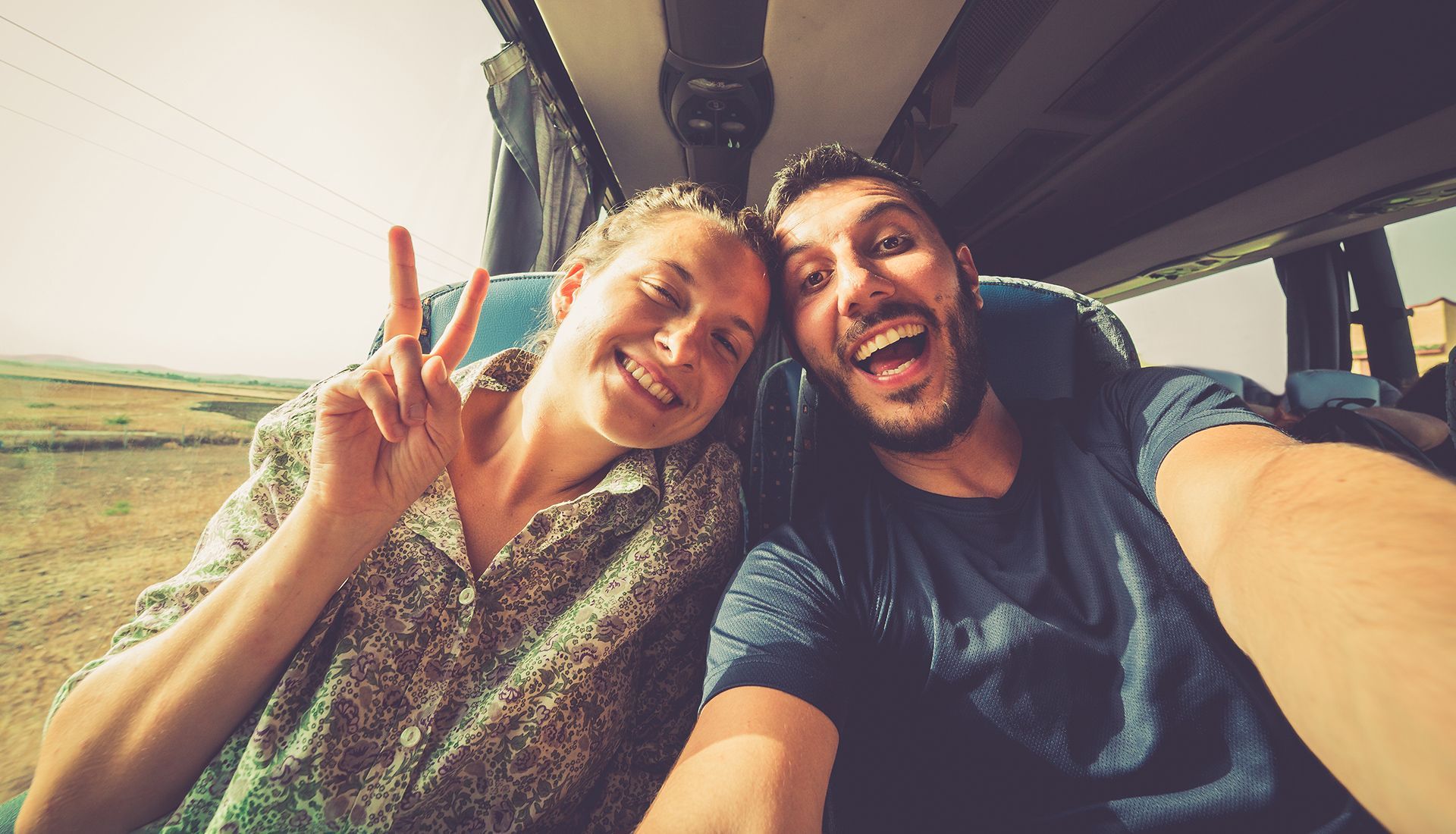 Couple smiles and takes selfie, woman makes peace sign.