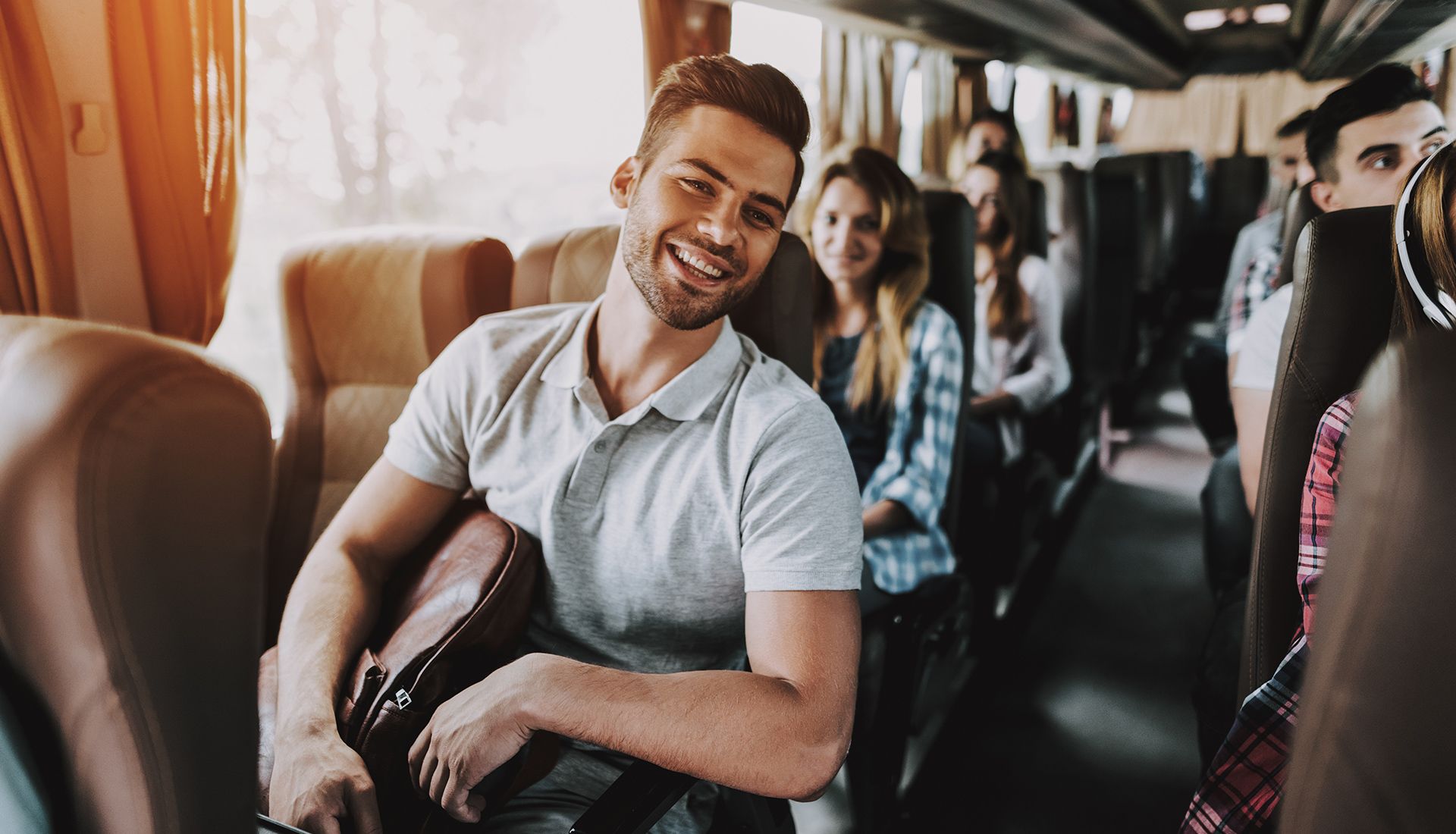 Man smiling and holding bag on a bus, surrounded by other passengers.