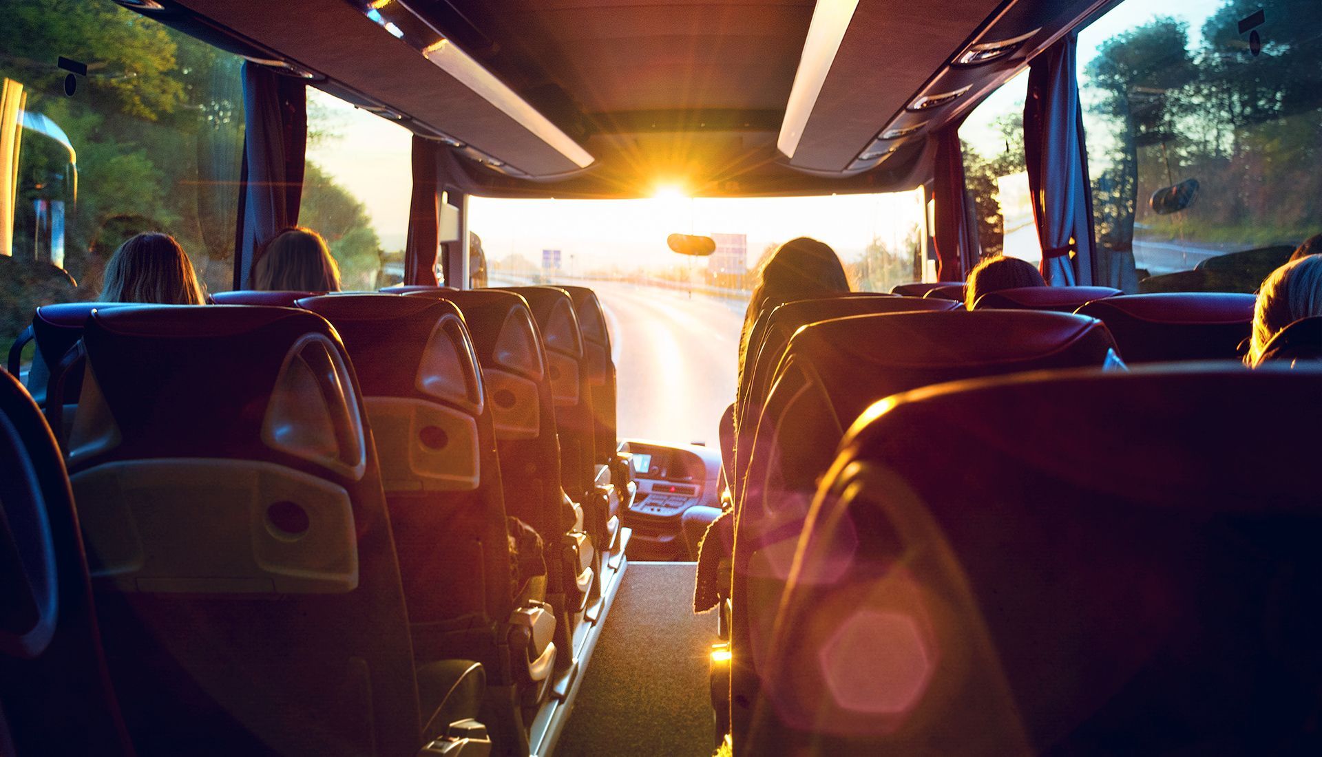 Interior of a bus, view toward the front window, with passengers in seats; sunlight streaming in.