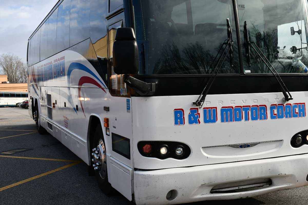 White B&W Motor Coach bus parked in a parking lot. Blue, red accents, windshield wipers.