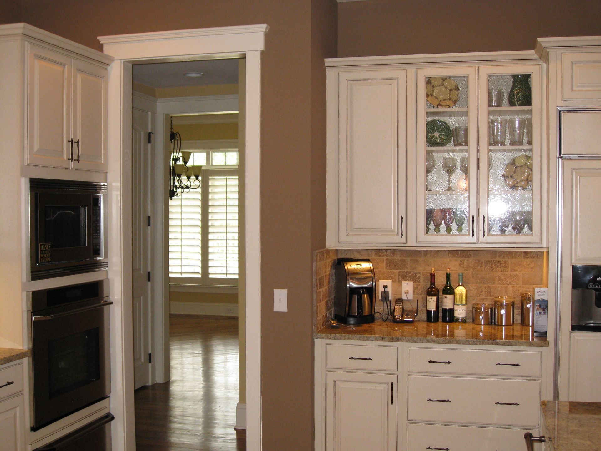 Bright kitchen with cream cabinets, double oven, glass-front cupboards, and a granite coffee nook.