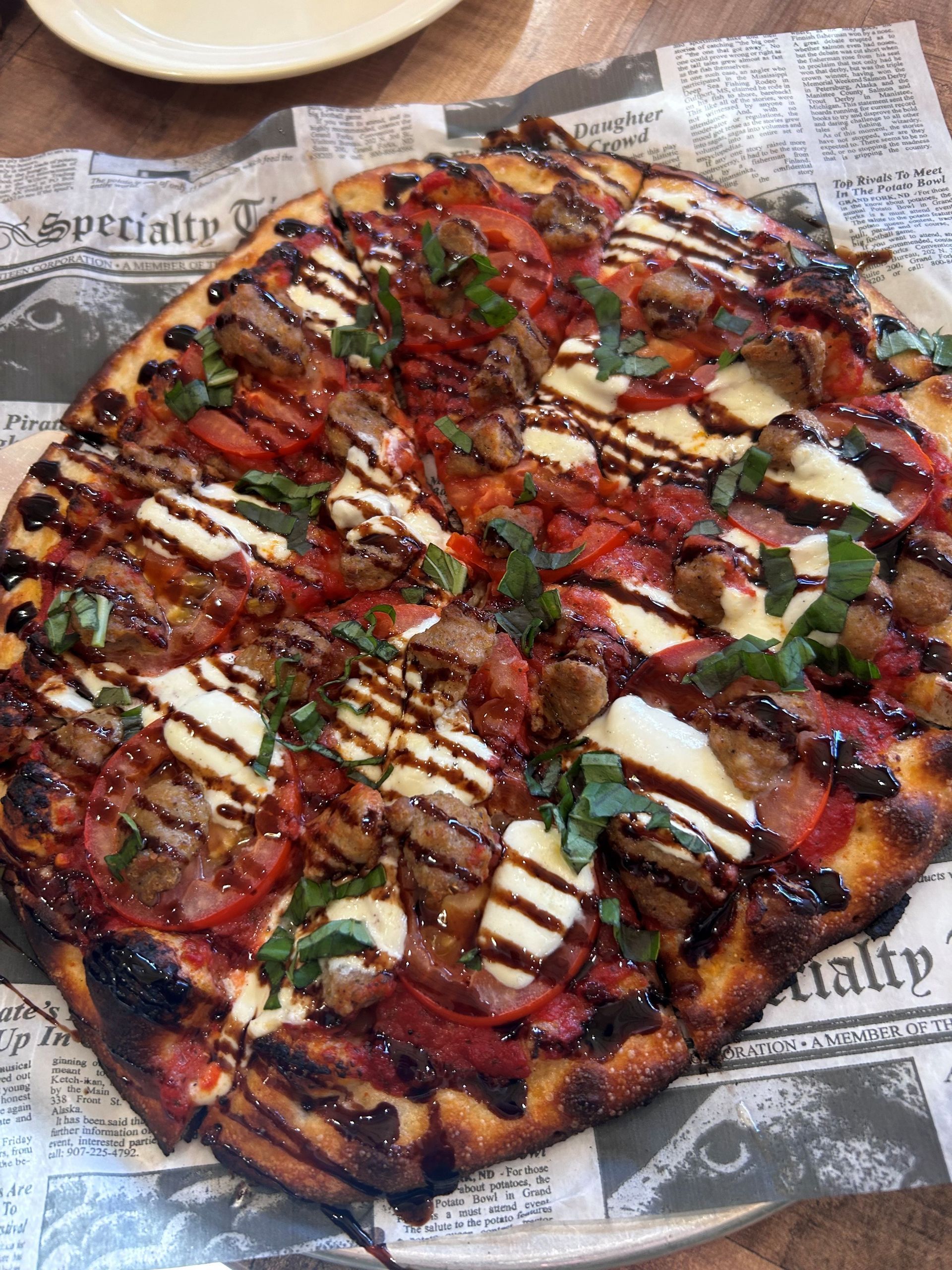 A pizza with tomatoes , cheese and basil on a table.
